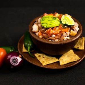 Menu A colorful bowl of Mexican bean salsa topped with avocado and lime, surrounded by fresh ingredients.