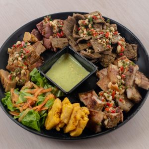 Menu Assorted grilled meats with fresh salad and dip on a black plate.