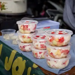 Colorful fruit salad cups with cream on display at an outdoor market stand.