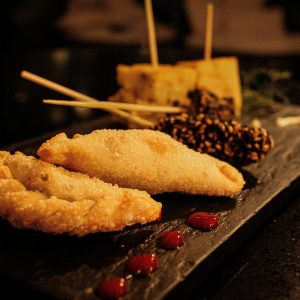 Menu Delicious gourmet dish featuring fried empanadas and skewers on a dark serving platter.