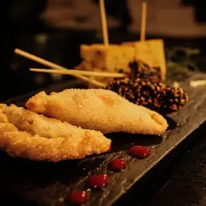 Menú Delicious gourmet dish featuring fried empanadas and skewers on a dark serving platter.