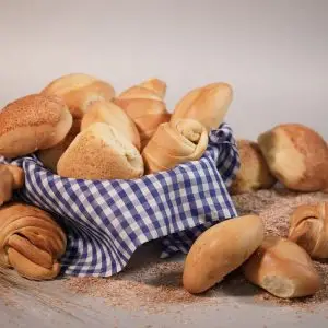 Menú A variety of freshly baked bread rolls in a checkered basket on a wooden surface.
