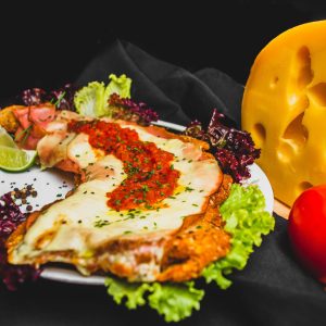 Delicious breaded cutlet topped with cheese and herbs, served with fresh salad, tomato, and lime wedge.